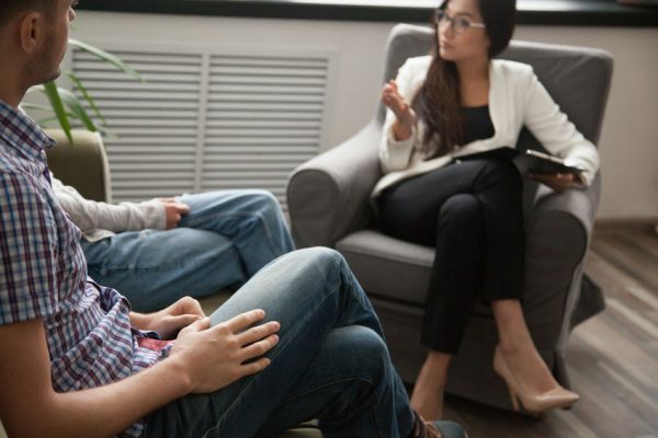 Asian psychologist counseling talking to unhappy couple in office, family counselor sexologist sitting in chair consulting family during therapy session, marriage and sexual problems solution concept